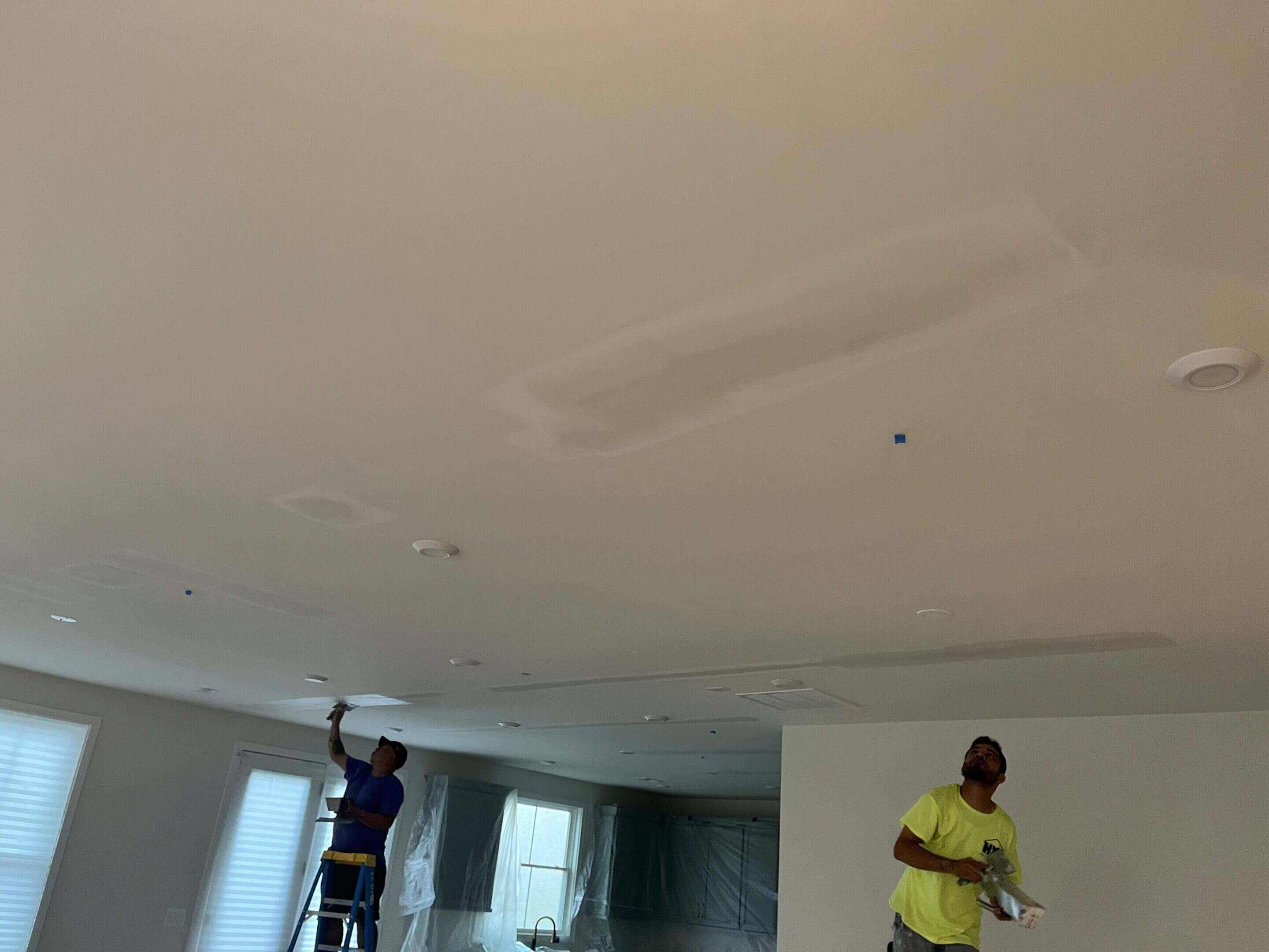 Two workers repairing a ceiling in a residential room.