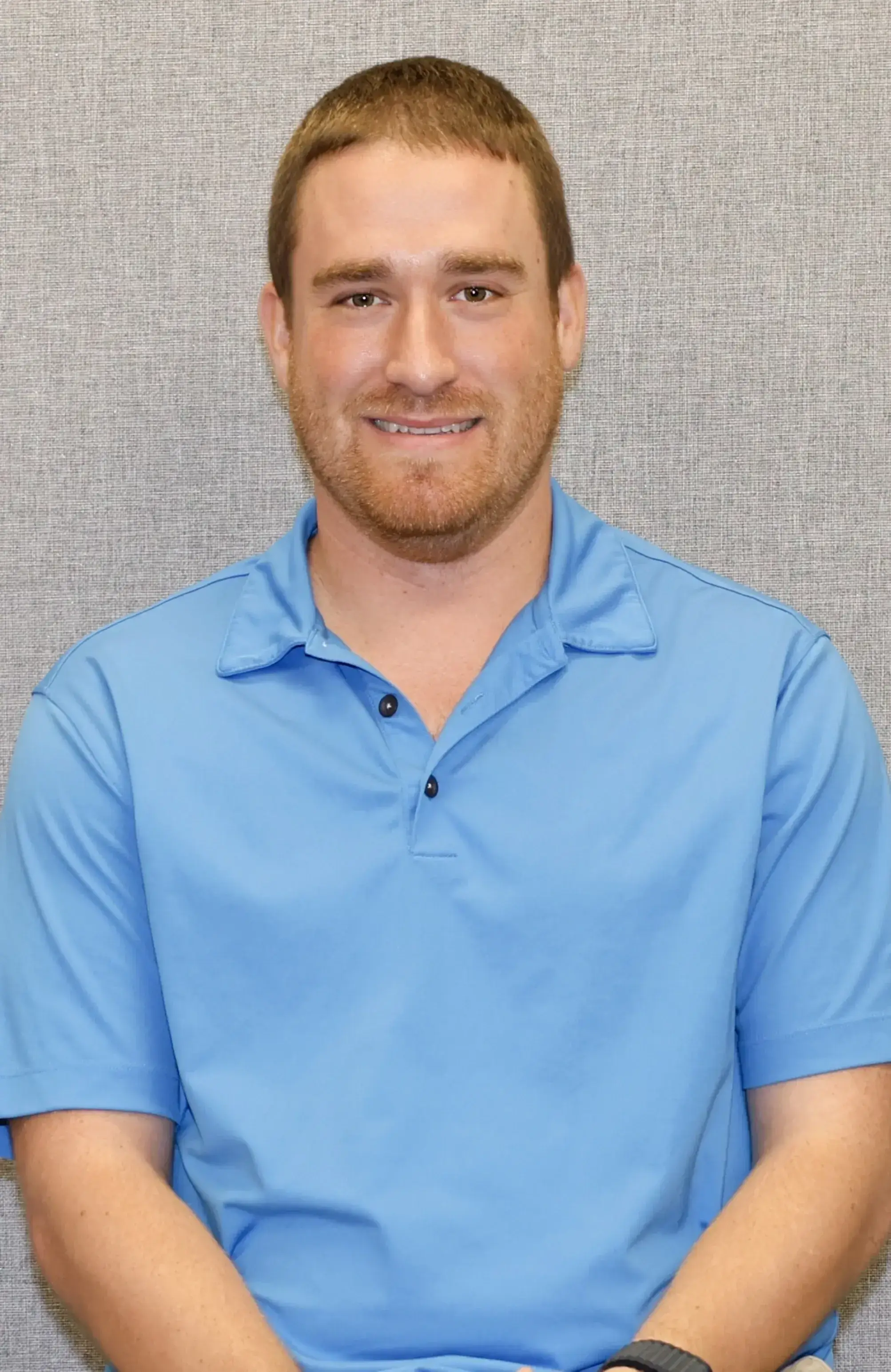 Man in a light blue polo shirt smiling at the camera.