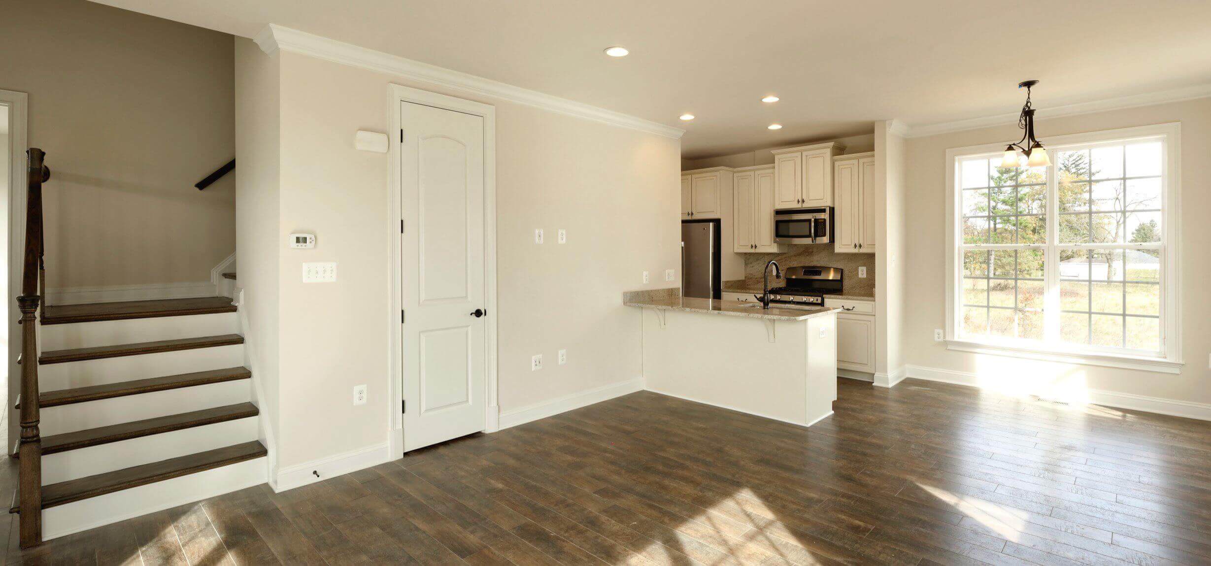 Empty modern kitchen with white cabinets and wooden flooring.